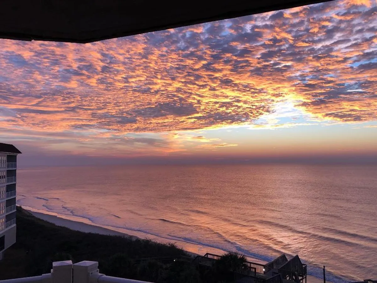 A breathtaking view of the ocean at sunset with gentle waves and a dramatic sky filled with colorful clouds. The shoreline stretches into the distance, creating a peaceful and inspiring scene ideal for leisurely walks or shared contemplation.