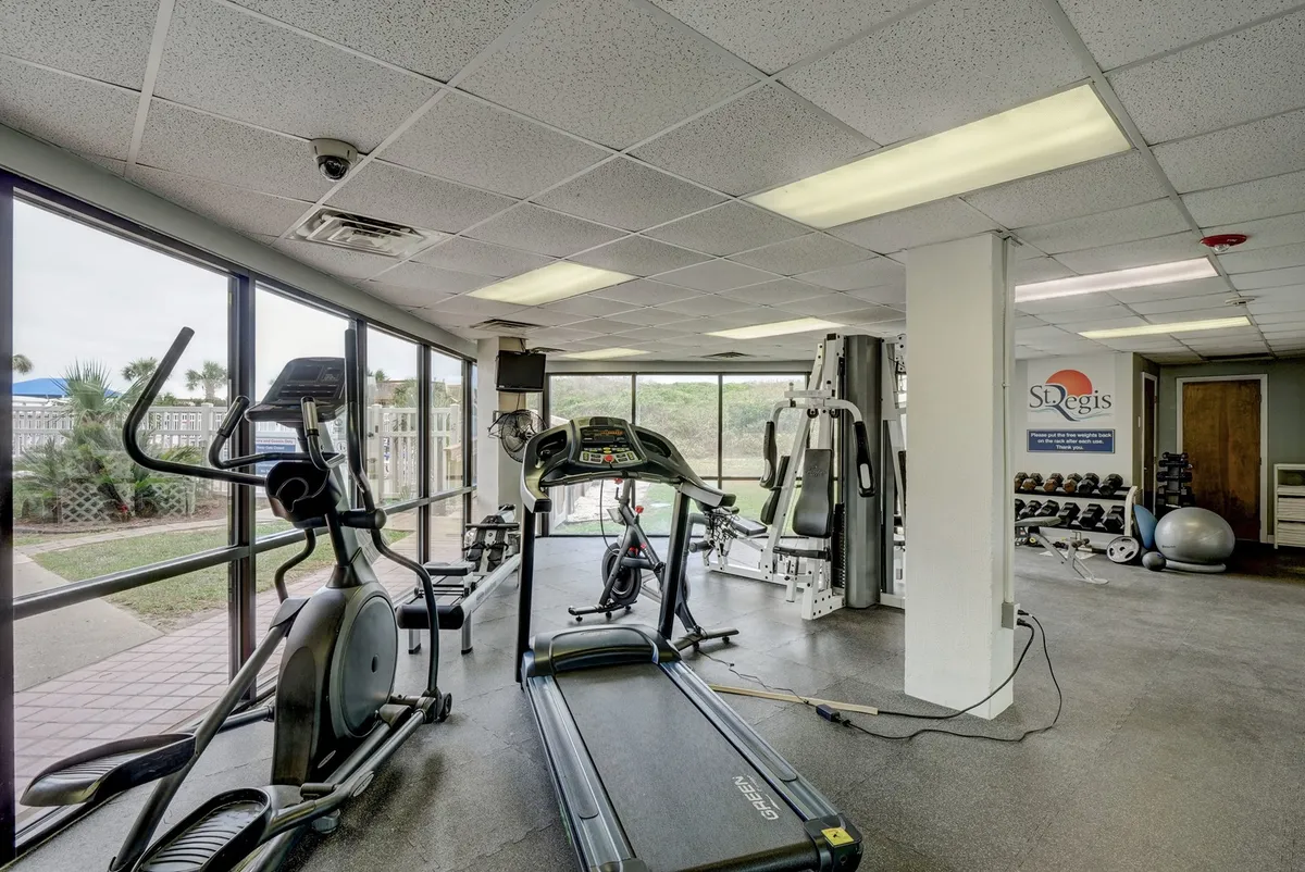 A modern fitness center featuring treadmills, elliptical machines, and strength training equipment. Large windows provide natural light and offer a view outside, creating an inviting, energizing space for workouts.