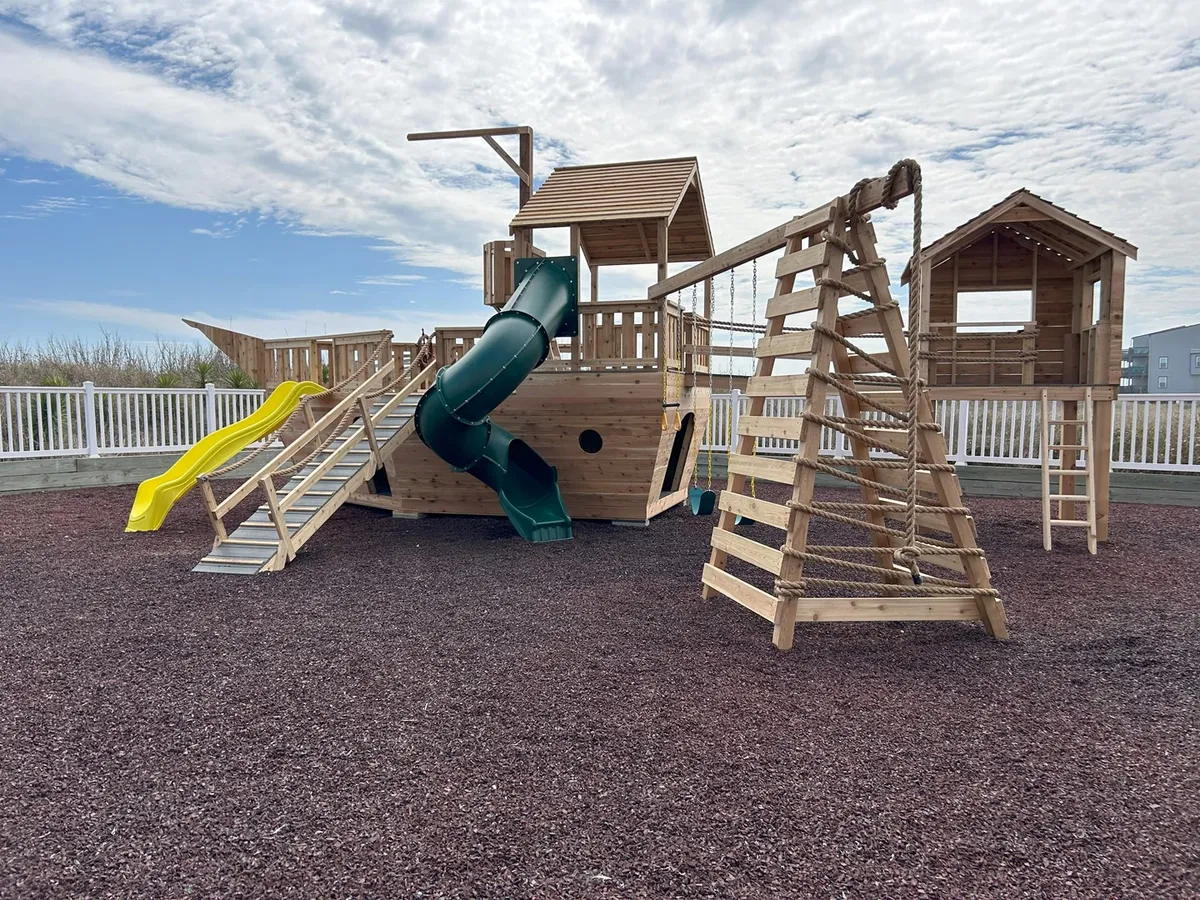 A colorful playground structure featuring slides, climbing ropes, and a wooden playhouse. The play area is lively and designed to spark children's imagination, inviting families to enjoy outdoor fun together.