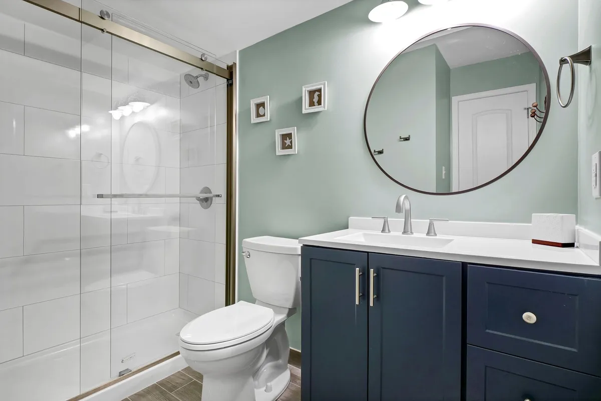 A renovated bathroom showcasing a modern walk-in shower, a sleek round mirror above a streamlined vanity, and a fresh, clean atmosphere with tranquil touches.