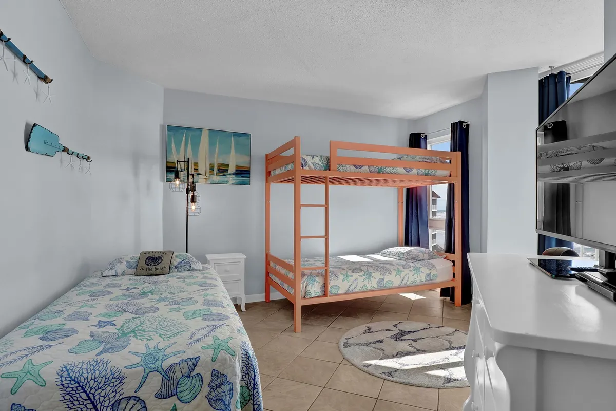 An inviting guest bedroom with a playful twin-over-twin bunk bed and an additional single bed, accented by creative wall art and a cheerful light fixture. The space feels bright and ideal for kids or friends sharing a room.