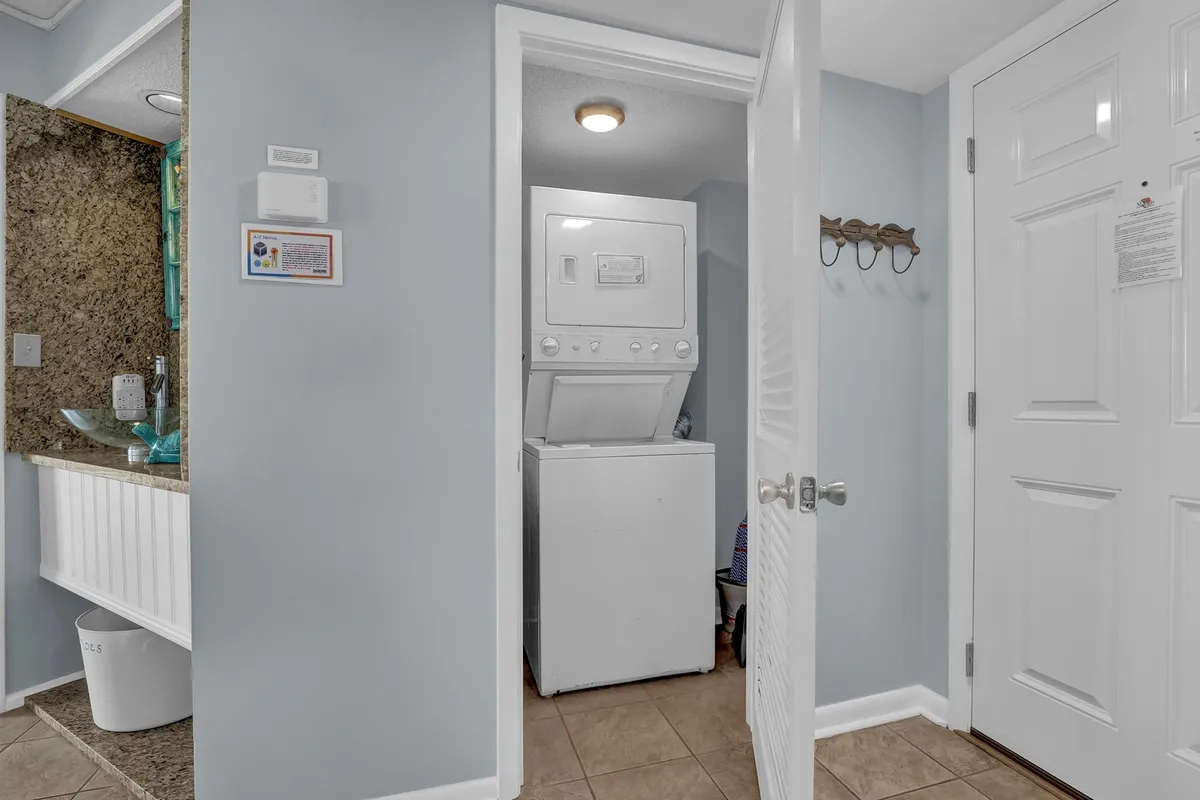 This image features a practical laundry space with a washer and dryer set neatly into a granite countertop area, wall hooks for organization, and a generally orderly ambiance. The setting conveys the satisfaction and ease of handling linens or laundry within the condo itself.